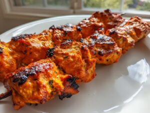 Close-up of vibrant orange, charred Bang Bang Chicken Skewers Moribyan resting on a white plate.