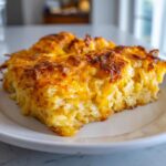 A close-up of a cheesy, golden-brown slice of the best hashbrown casserole served on a white plate.