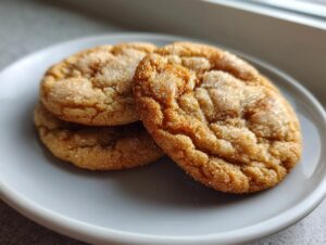 Three soft, crinkled brown butter sugar cookies coated in sparkling sugar resting on a light gray plate.