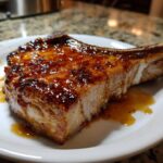 A thick, bone-in pork chop covered in a shiny, caramelized brown sugar glaze, served on a white plate.