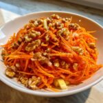 Close-up of a vibrant carrot apple walnut salad topped generously with whole walnuts and poppy seeds.