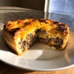 A golden-brown, flaky crust cheeseburger pie with crust cut in half, revealing a savory ground beef and cheese filling.
