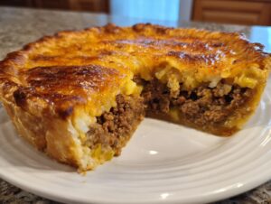 A close-up of a slice removed from a baked cheeseburger pie with crust, showing the ground beef filling and cheesy topping.