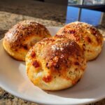 Three golden-brown cheesy garlic pepperoni pizza bombs topped with grated Parmesan cheese, resting on a white plate.