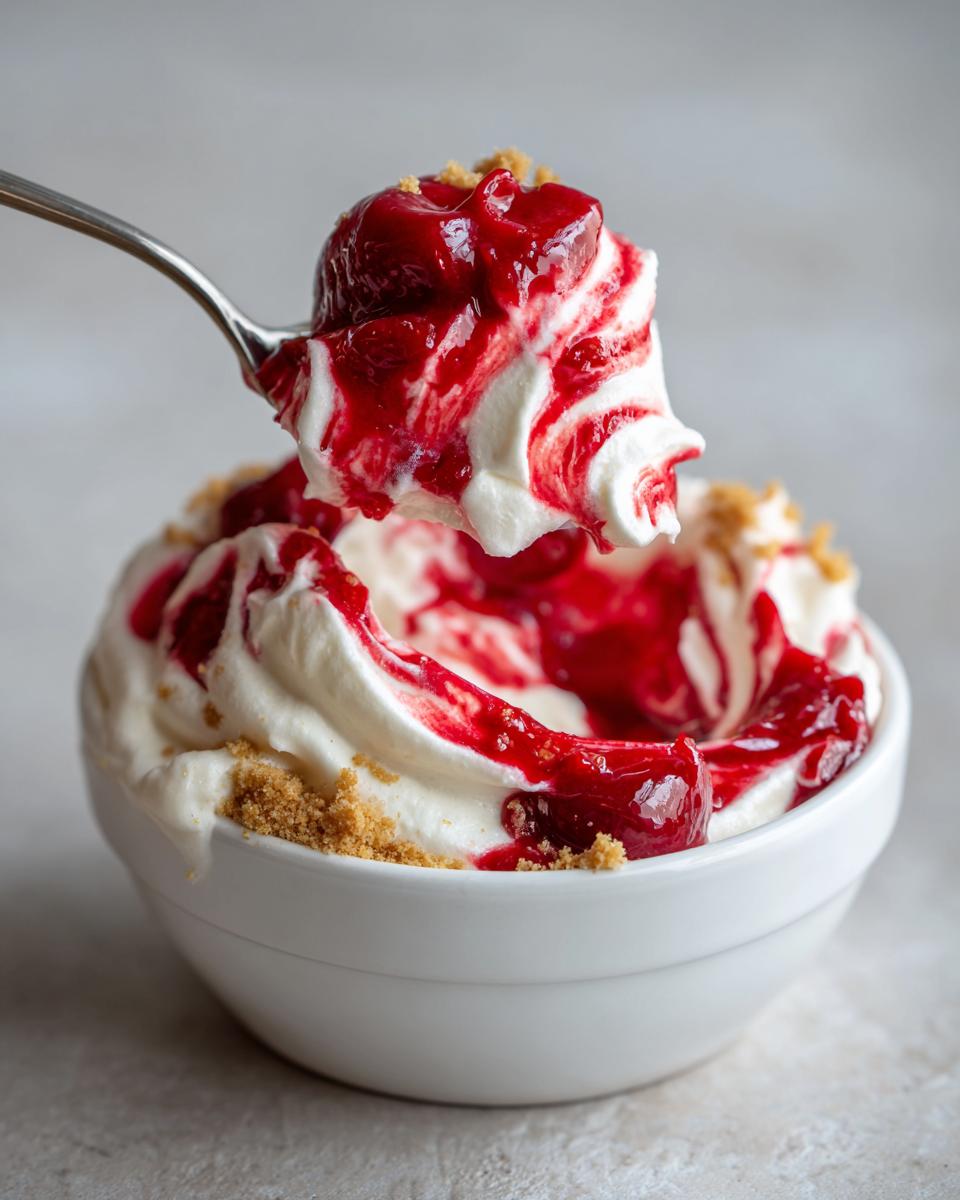 A spoonful of creamy white cherry cheesecake fluff topped with bright red cherry sauce being lifted from a white bowl.