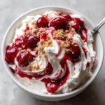 A close-up of creamy white cherry cheesecake fluff topped with bright red cherry pie filling and graham cracker crumbs.