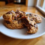 Close-up of chewy salted caramel cookies, one broken open revealing gooey caramel and topped with sea salt.