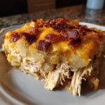 A close-up slice of rich chicken bacon potato bake featuring shredded chicken, potatoes, melted cheddar, and crispy bacon bits.