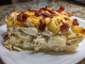 Close-up of a serving of chicken bacon potato bake showing layers of shredded chicken, potatoes, and a cheesy, bacon-topped crust.