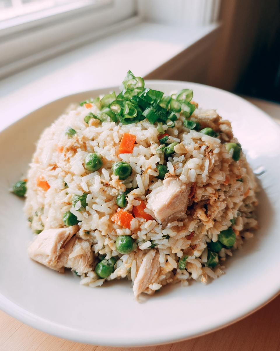 A mound of delicious chicken fried rice mixed with peas and carrots, topped with fresh green onions.