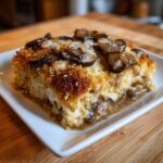 A square serving of baked chicken marsala casserole topped with melted cheese and sautéed mushrooms.