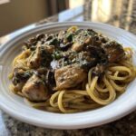 A close-up of a white bowl filled with chicken marsala pasta, featuring creamy sauce, chicken pieces, and dark mushrooms.