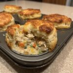 A close-up view of one of the chicken pot pie biscuit cups broken open to show the creamy chicken and vegetable filling.