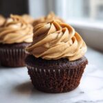 A close-up of a decadent chocolate peanut butter cupcakes topped with a swirl of creamy peanut butter frosting.