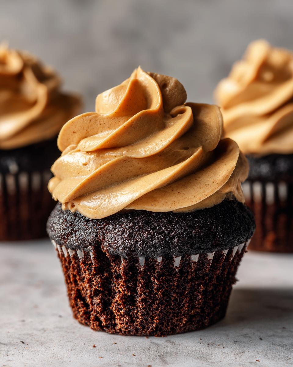 A close-up of a rich chocolate cupcake topped with a swirl of creamy peanut butter frosting, part of a batch of chocolate peanut butter cupcakes.