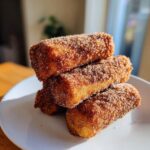A stack of four golden brown cinnamon french toast roll ups heavily coated in sparkling cinnamon sugar mixture.