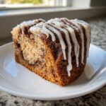 A close-up of a moist slice of cinnamon roll cake recipe topped with thick white icing drizzle.