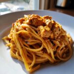 A close-up of creamy cowboy butter chicken linguine tossed in a rich orange sauce, served on a white plate.