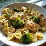 Close-up of cowboy butter lemon bowtie chicken with broccoli in a creamy sauce served in a white bowl.