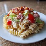 A serving of creamy club sandwich pasta salad made with rotini pasta, topped with lettuce, tomato, ham, and crispy bacon bits.