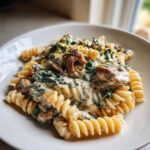 A close-up of creamy ricotta chicken pasta made with fusilli, spinach, and topped with lemon zest.