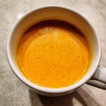 Close-up overhead view of vibrant orange squash soup served hot in a white ceramic mug.