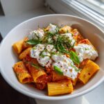 A close-up of creamy tomato pasta with burrata, garnished with fresh basil and chili flakes.