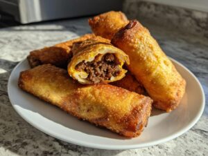 A plate piled high with golden brown, crispy cheeseburger egg rolls, one cut open showing the savory ground beef filling.