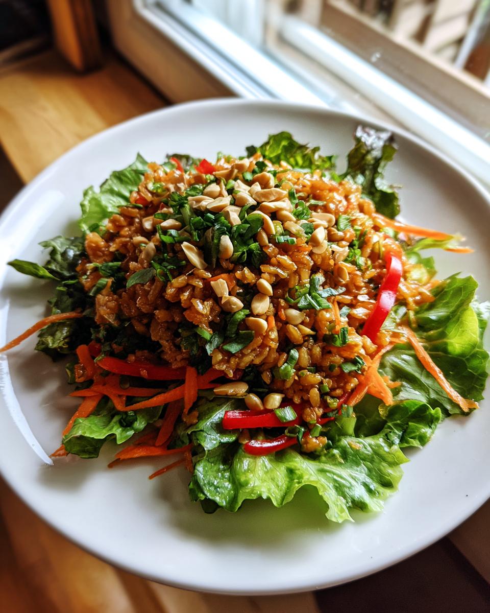 A vibrant serving of crispy rice salad with peanut sesame dressing, topped with peanuts and chives, resting on lettuce.