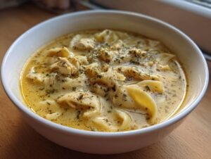 Close-up of a white bowl filled with crock pot creamy chicken parmesan soup, featuring shredded chicken and egg noodles.