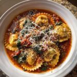 Close-up of a bowl of rich crockpot ravioli lasagna soup topped with shredded Parmesan cheese and black pepper.