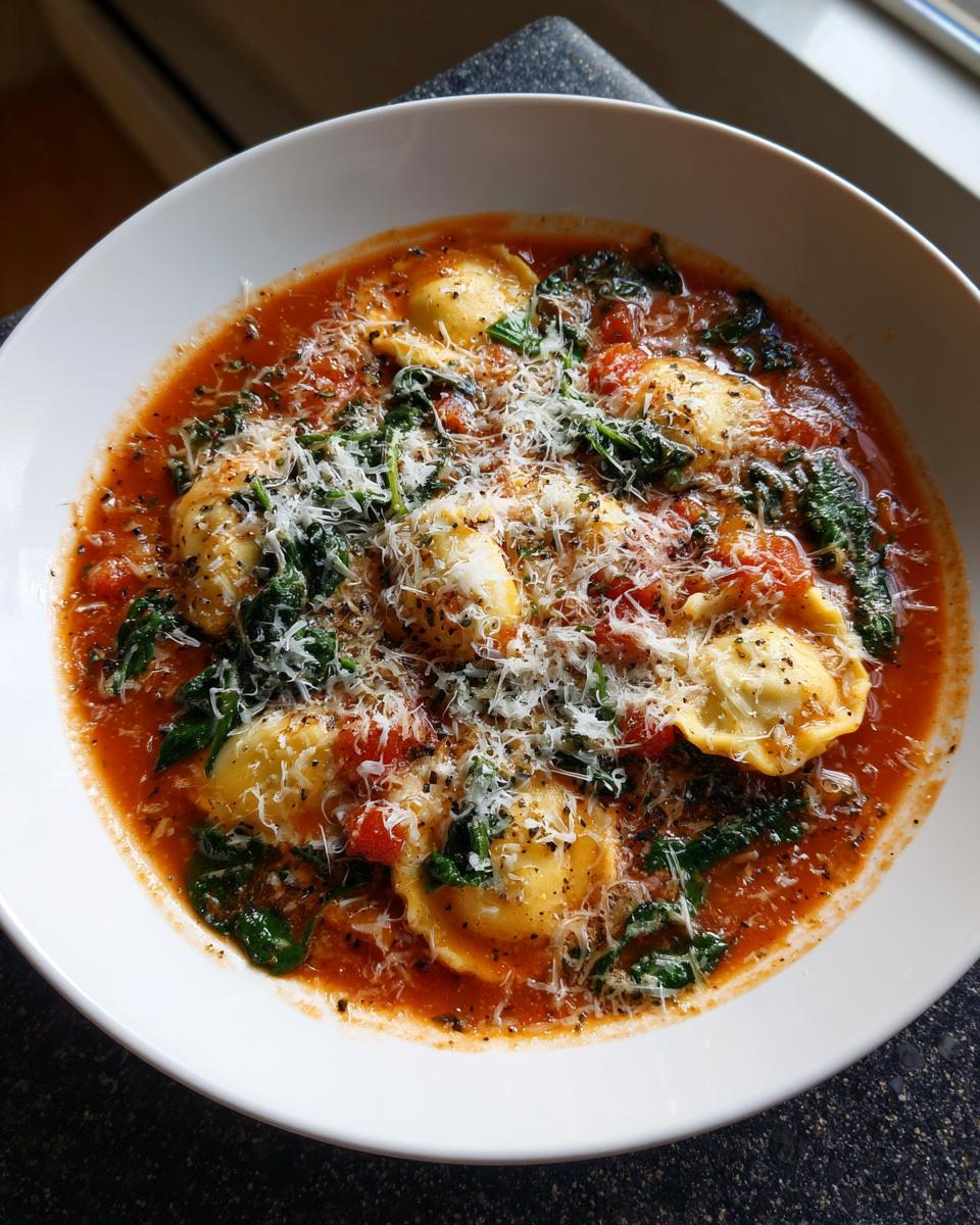 Top-down view of a white bowl filled with crockpot ravioli lasagna soup, featuring ravioli, spinach, tomato broth, and grated parmesan.