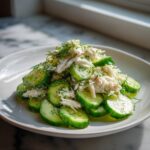 A mound of cucumber salad with crab meat and fresh dill served on a white plate.