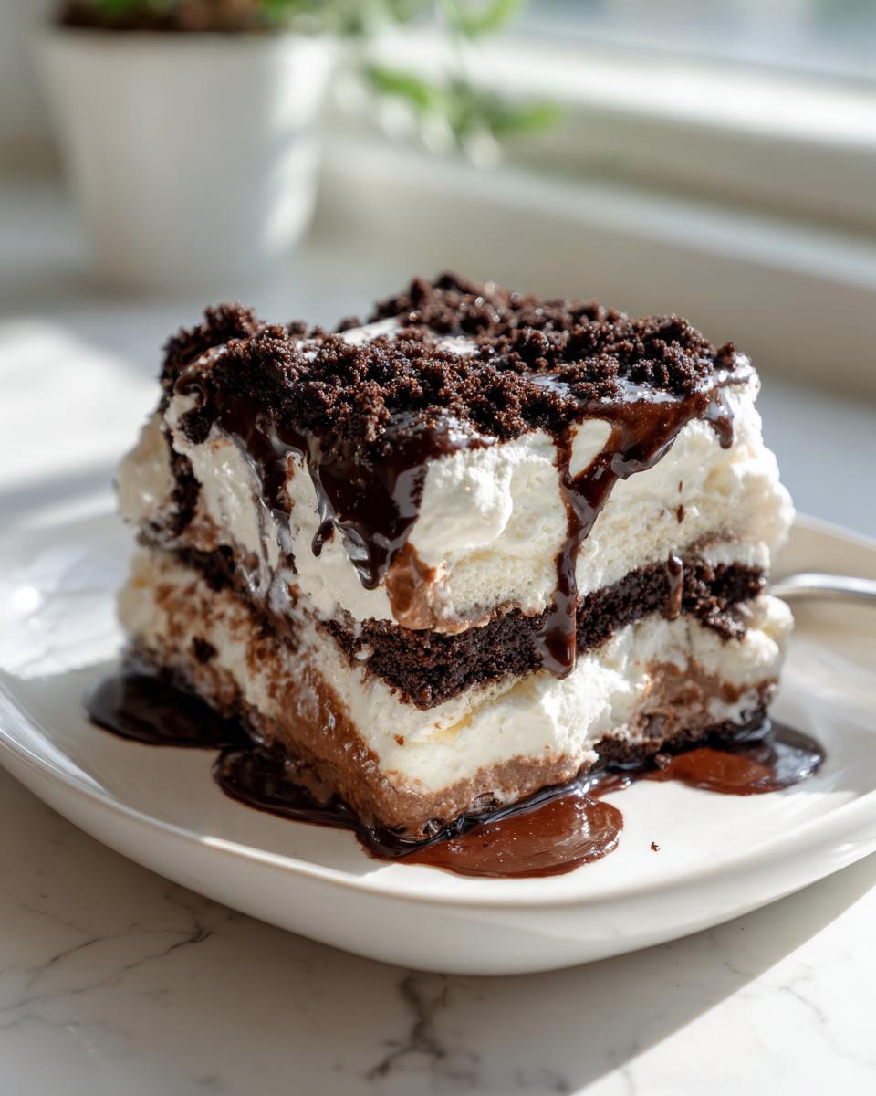 A delicious slice of layered dairy queen ice cream cake topped with whipped cream, chocolate crumbs, and fudge sauce.