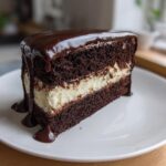 A decadent slice of ding dong cake featuring dark chocolate layers, white cream filling, and dripping chocolate ganache.
