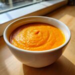Close-up of a white bowl filled with smooth, bright orange easy butternut squash soup.