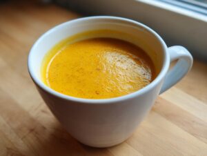 Close-up of vibrant orange easy butternut squash soup served in a white mug on a wooden surface.