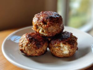 Three golden-brown, seared feta stuffed greek chicken meatballs stacked on a small white plate.