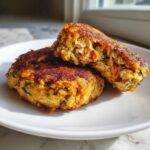 Close-up of two golden-brown baked salmon patties, one cut in half to show the flaky texture inside.
