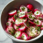 Close-up of thinly sliced radishes tossed in a light dressing and fresh green herbs, showcasing a vibrant radish salad.