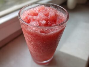 Close-up of a tall glass filled with icy, bright red frozen strawberry lemonade.
