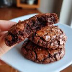A hand breaking one of the fudgy brownie mix cookies in half to show the rich, moist interior.