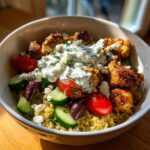 A vibrant garlic mediterranean chicken bowl featuring seasoned chicken pieces over quinoa, topped with tzatziki sauce, cucumbers, tomatoes, and olives.