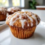 Close-up of a perfectly baked apple fritter muffins topped with a thick, white vanilla glaze drizzle.