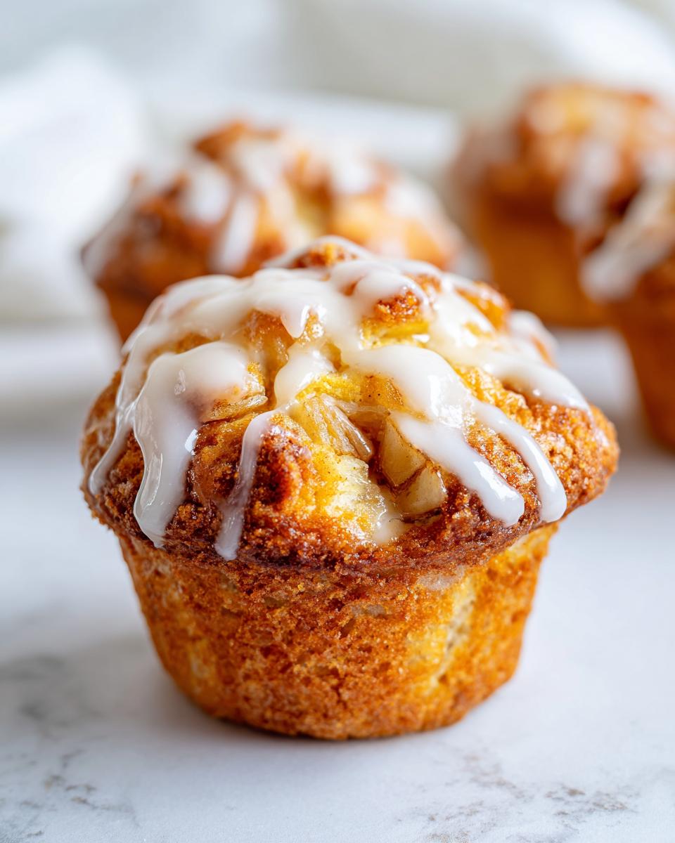 Close-up of a perfectly baked apple fritter muffin topped with a thick, sweet vanilla glaze.