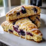 Close-up of three stacked lemon blueberry scones drizzled generously with white lemon glaze.