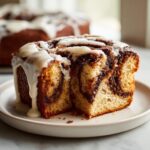 Close-up of a moist slice of gluten free cinnamon roll cake, showing the swirl pattern and thick white icing.