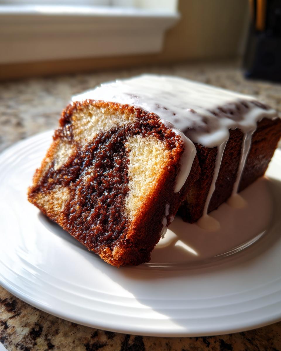 A close-up of a slice of gluten free cinnamon roll cake showing the cinnamon swirl and white glaze on a white plate.