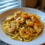 A close-up of glistening shrimp served over linguine pasta, prepared in the style of gordon ramsay's shrimp scampi.