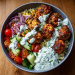 Overhead view of a bowl filled with greek chicken meatball bowls, featuring seared meatballs, quinoa, fresh vegetables, and creamy tzatziki sauce.
